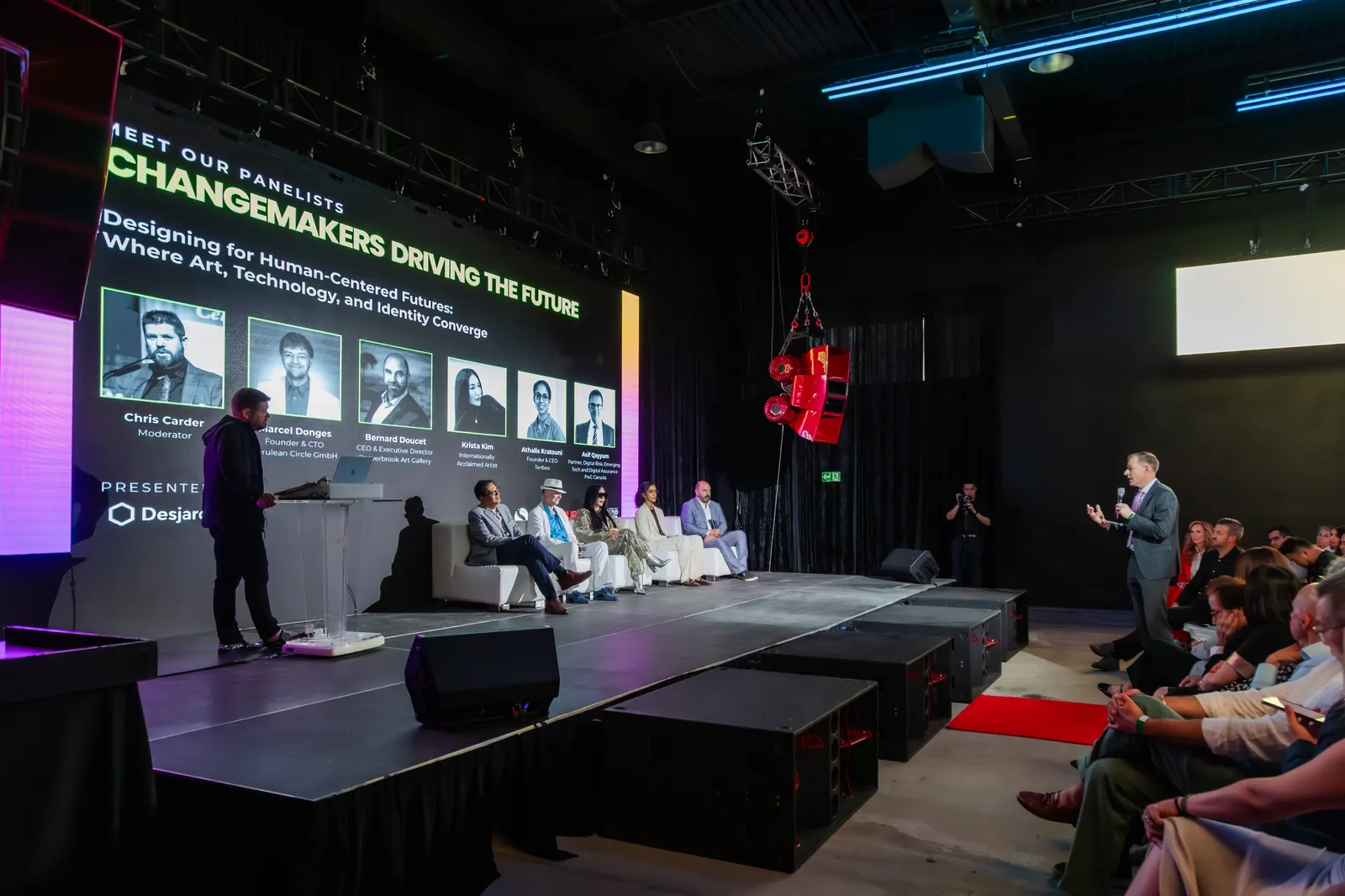 A panel on stage at a tech conference in Demo Room, speakers on the screen behind