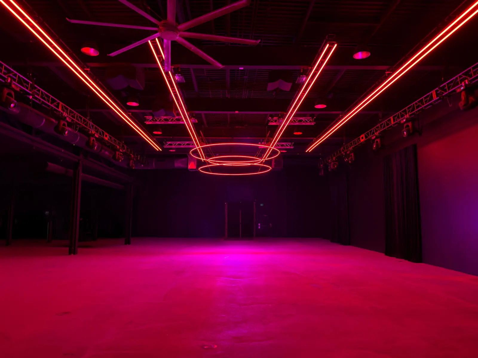 Demo Room's main floor empty, lit red and pink under suspended light rings