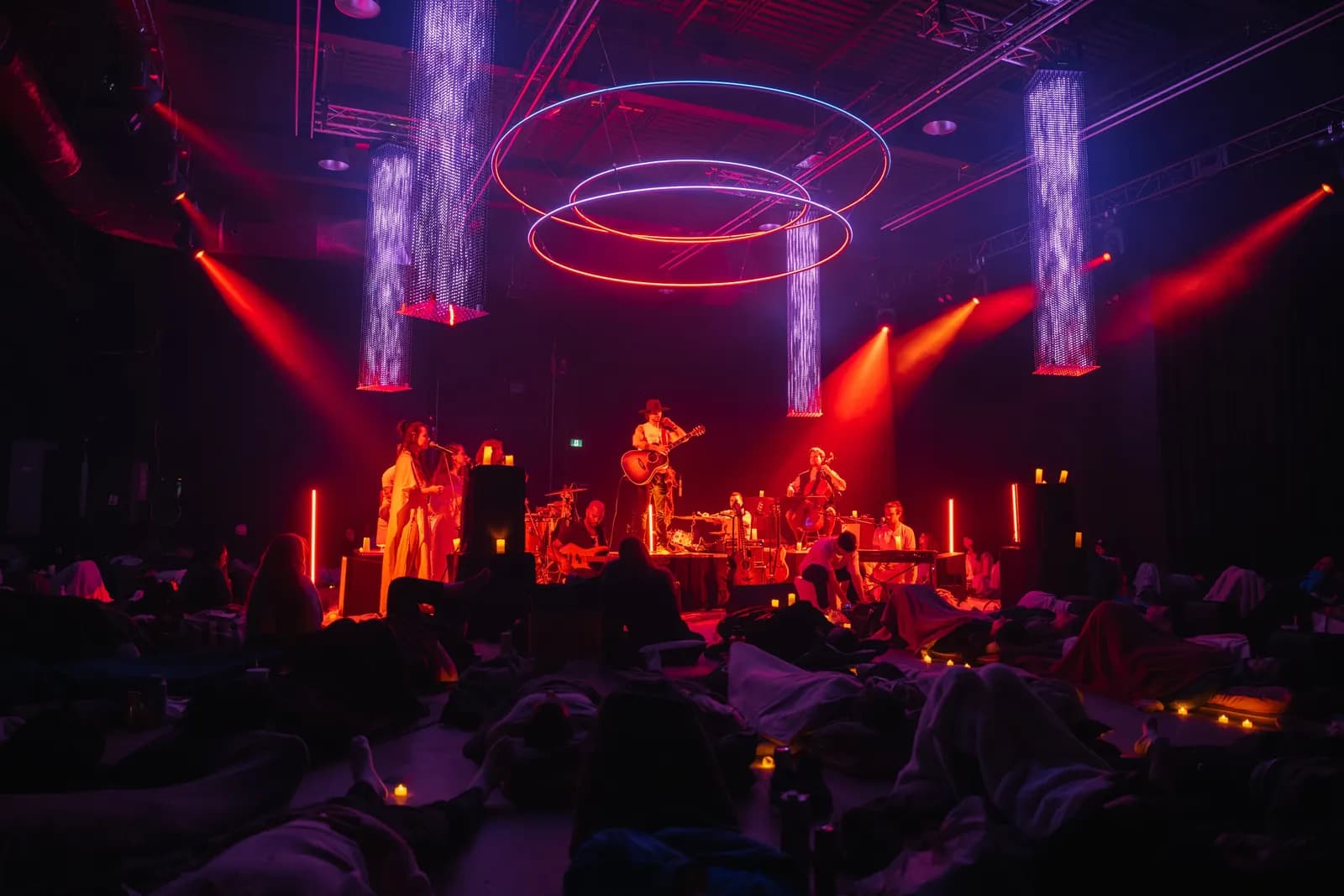 Musicians on stage under hanging light rings and red wash in Demo Room