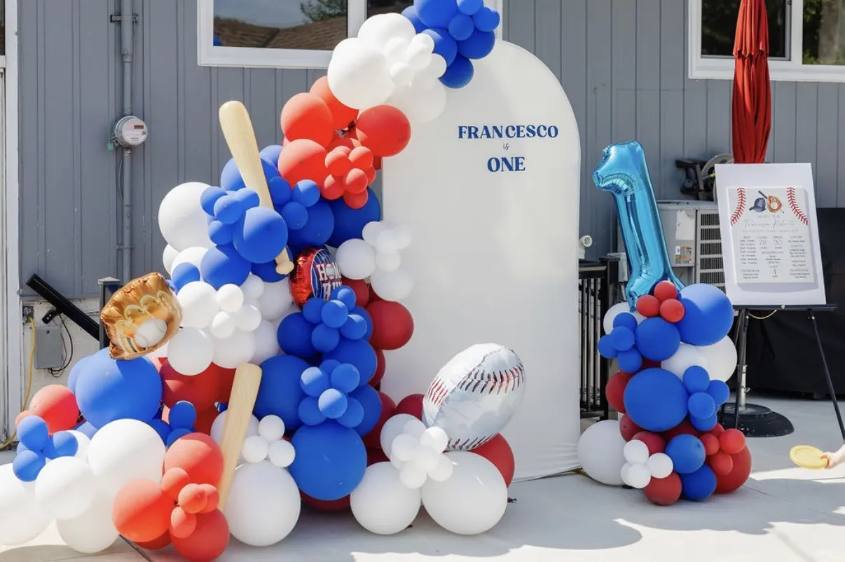 A red, white and blue balloon install with a baseball, bat and a first-birthday sign