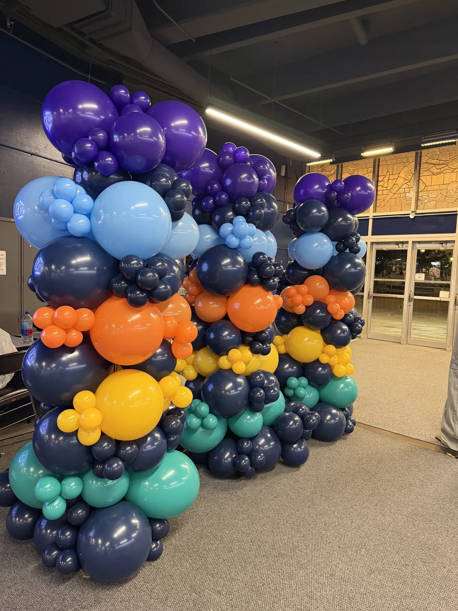 Balloon columns in orange, navy, teal and yellow along a stadium concourse