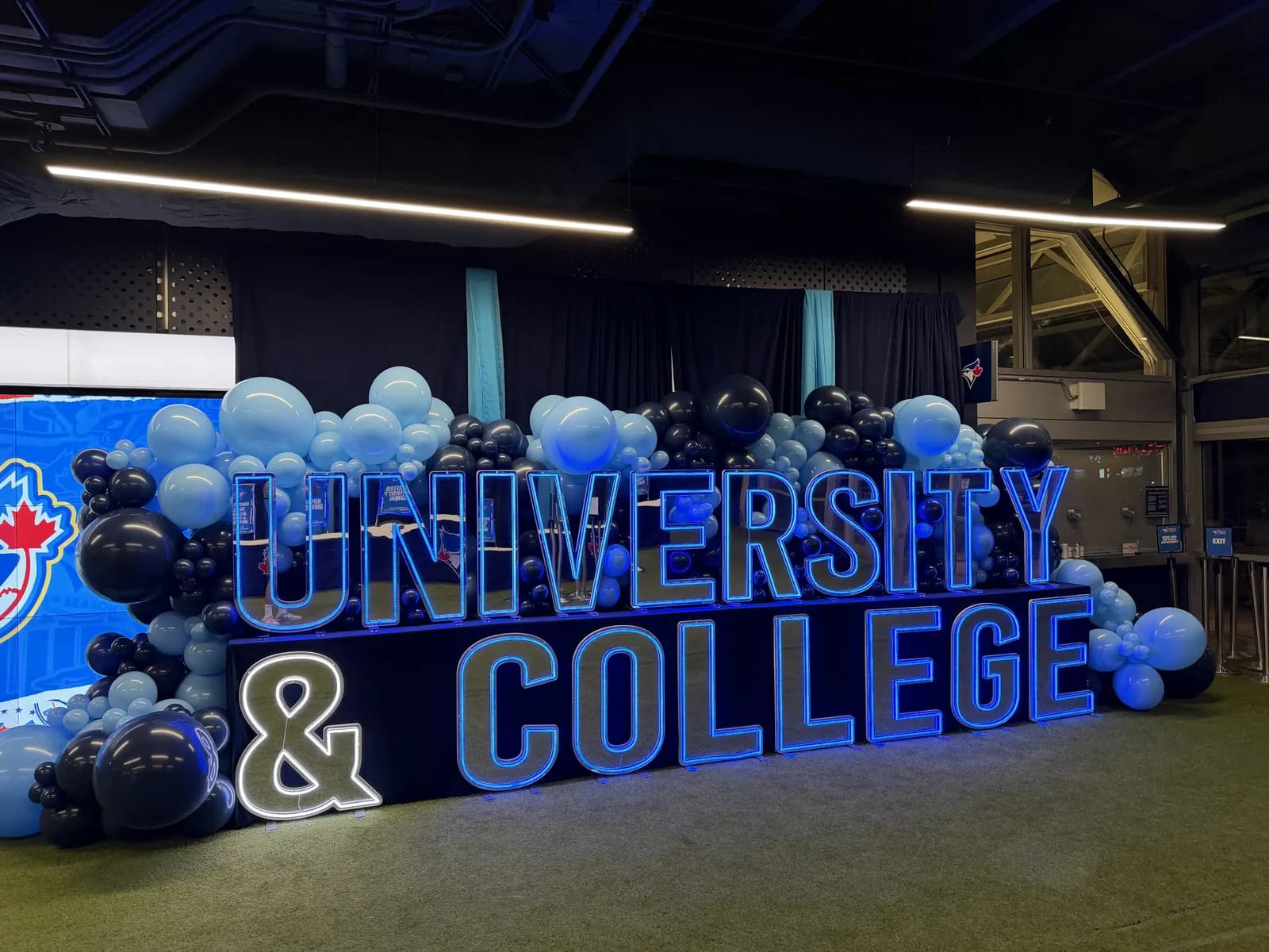 A balloon wall in navy and blue behind lit University & College letters