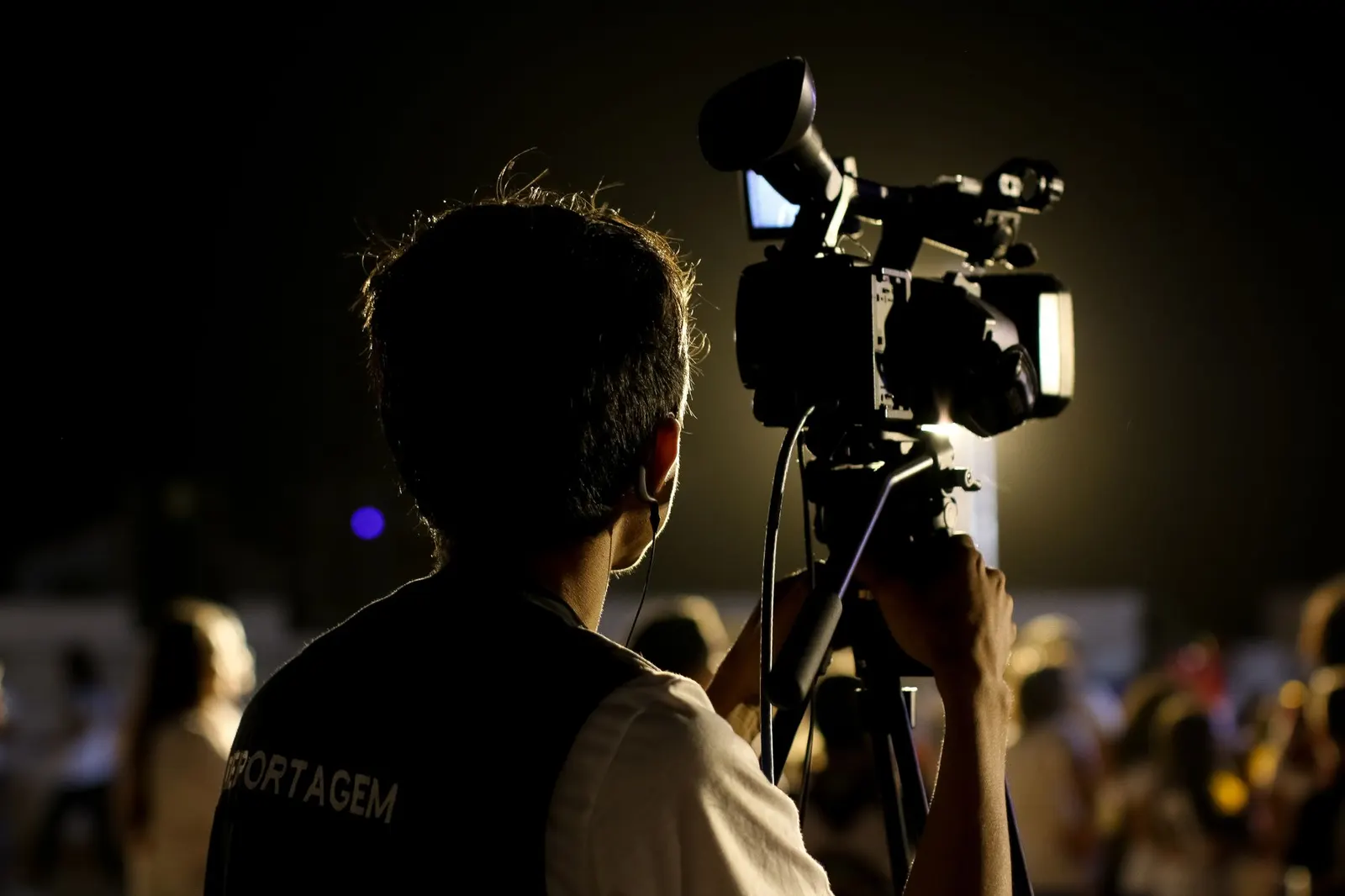 A camera operator filming an event at night, seen from behind