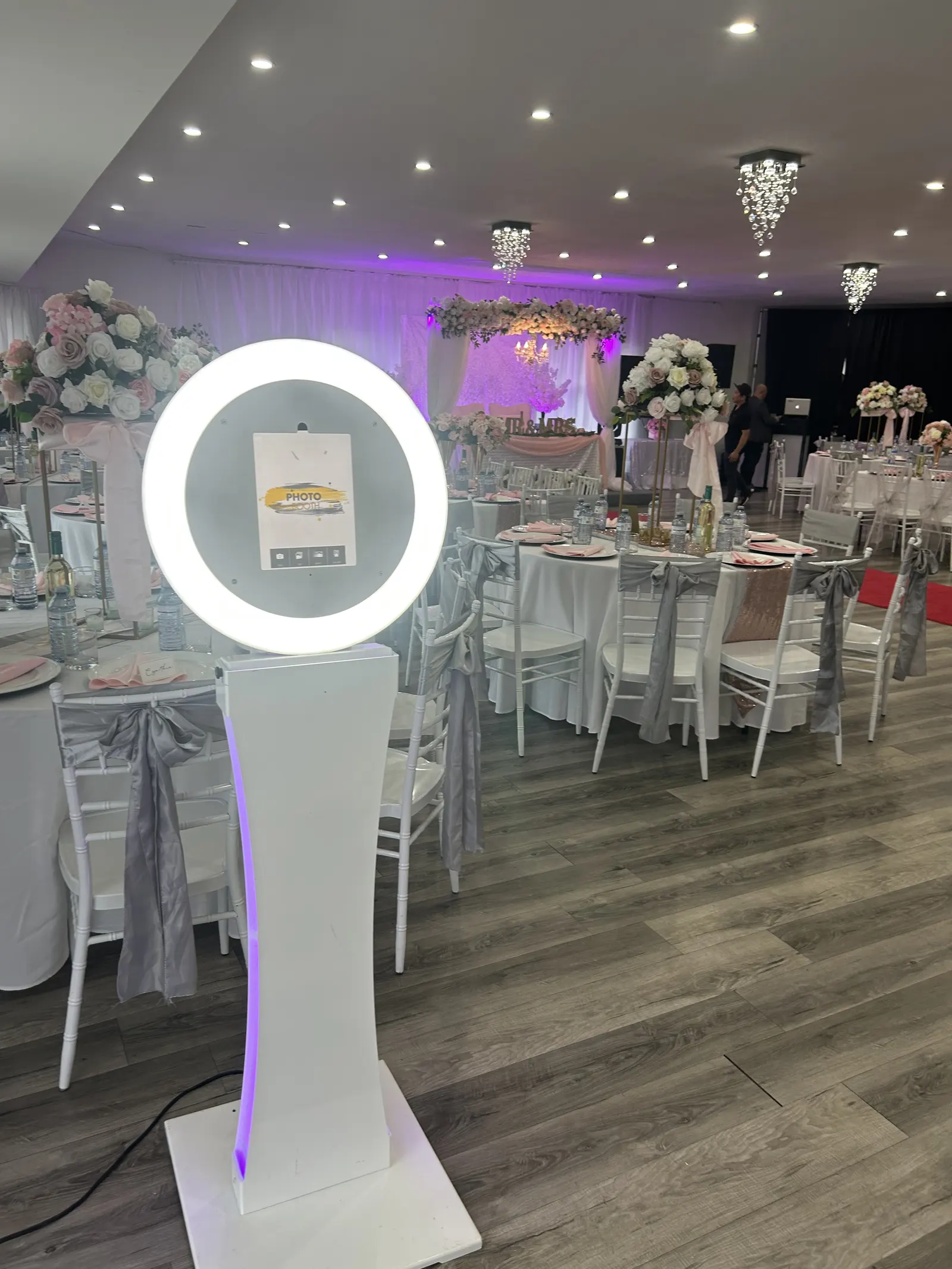 A white ring-light photo booth beside a dressed banquet hall