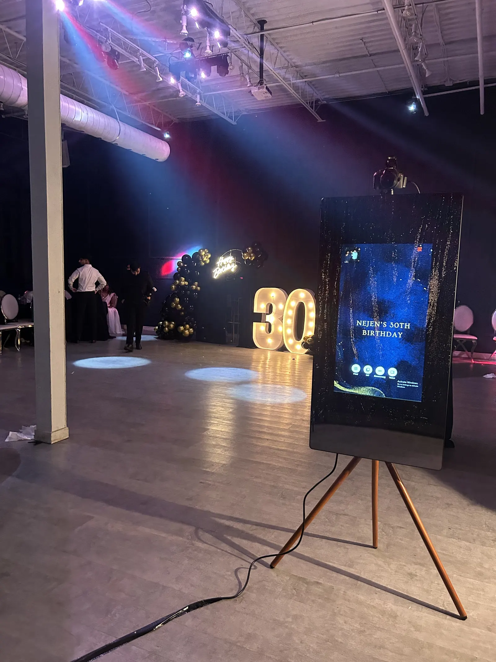 A screen photo booth on a tripod at a 30th birthday, lit numbers behind it